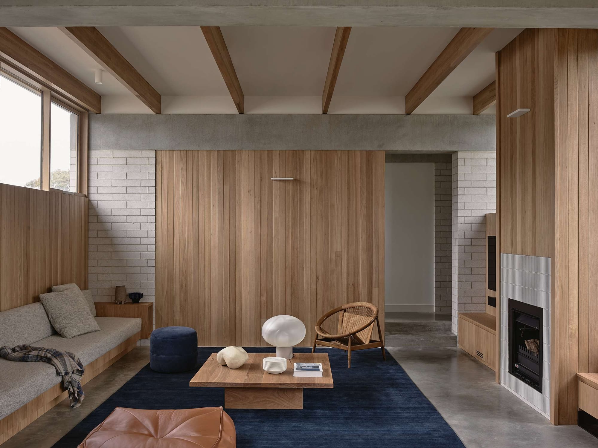 Home Pavilion by MRTN Architects. Sunken living space with concrete floors, timber clad walls and fireplace and navy rug. 