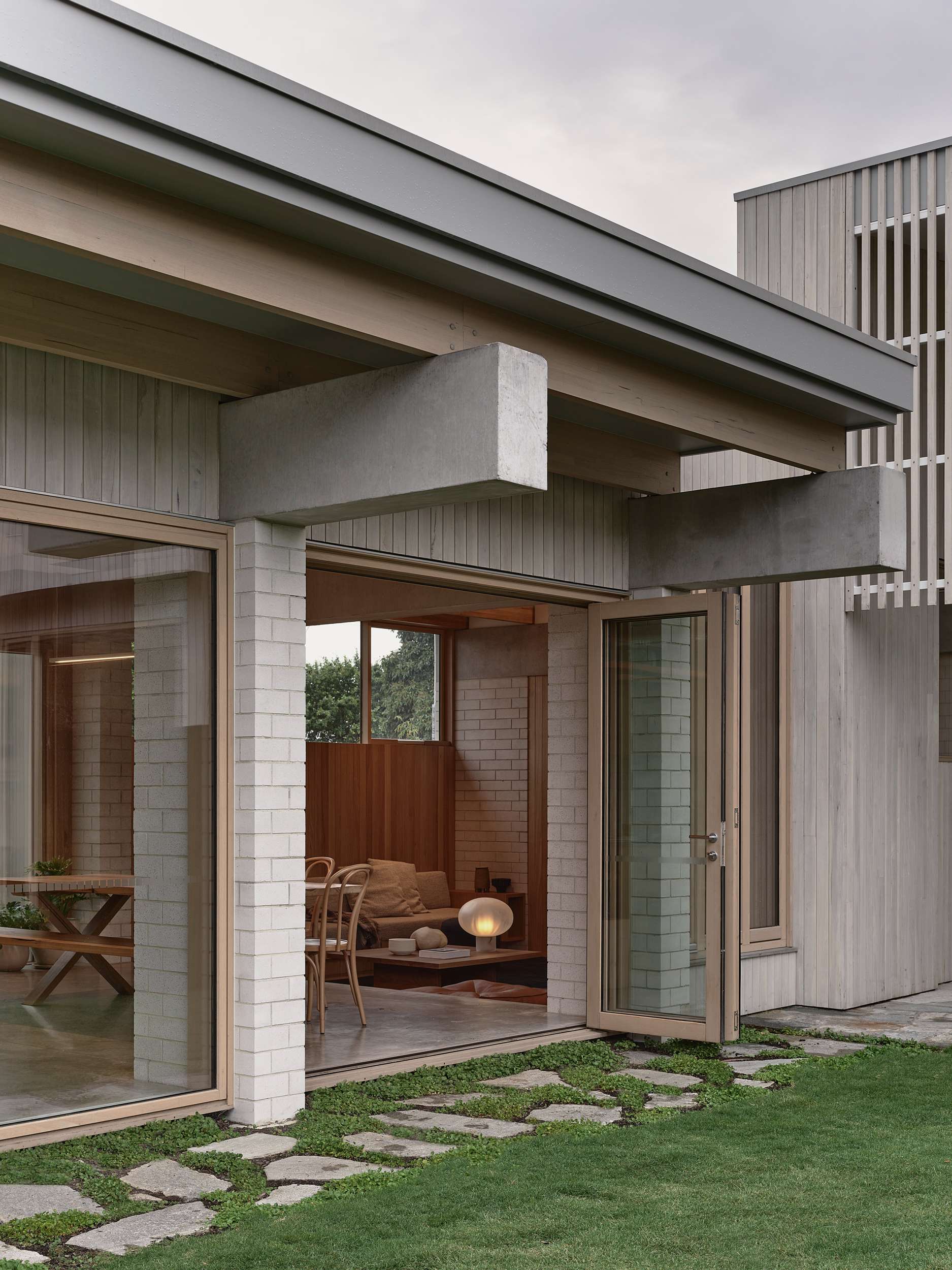 Home Pavilion by MRTN Architects. Folding timber-framed glass doors opening onto grassed courtyard, exposing interior with polished concrete floors and timber furnishings. 