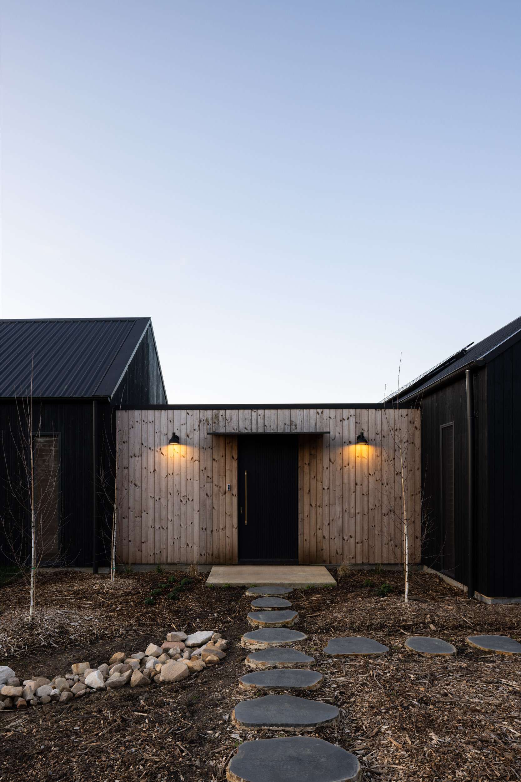 Birrigai House by Studio ERA. Photography by Simon Whitbread. Black timber clad walls, weathered timber deck, simple white metal chair and pitched black roof.