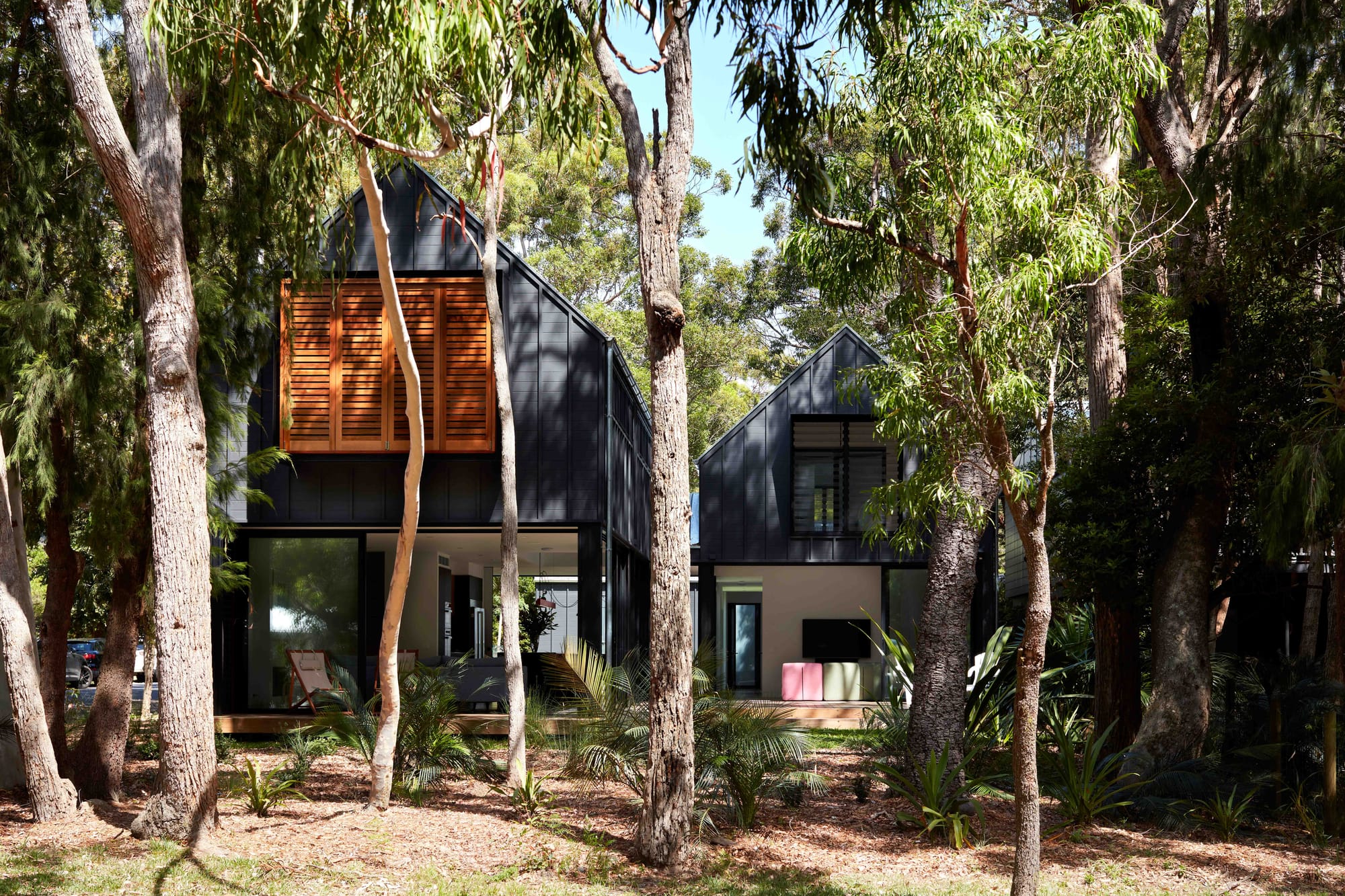 Pearl Beach II by COCO Architecture. Home in the forrest. Black-framed home with wooden shutters. 