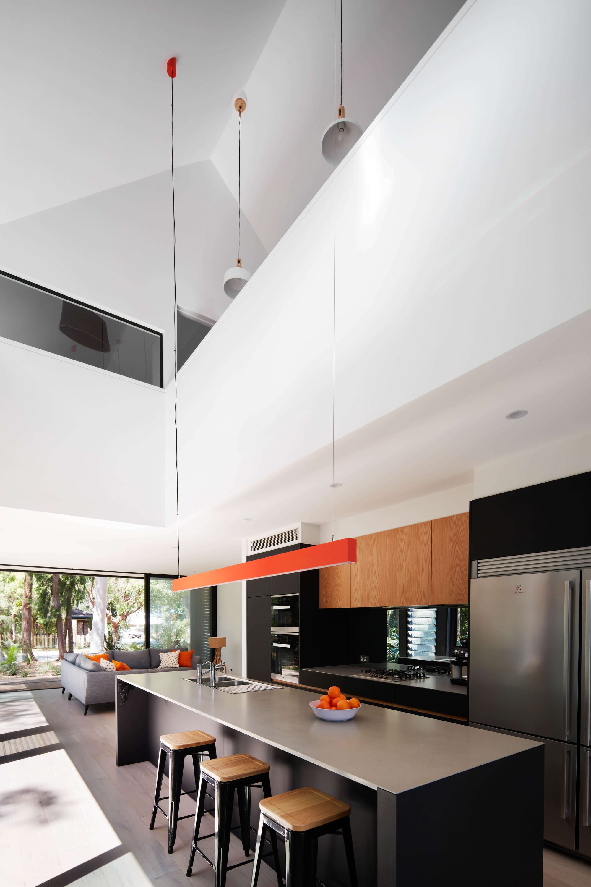 Pearl Beach II by COCO Architecture. Kitchen with large windows. Grey kitchen island with bar stools. Wooden cabinets and grey fridge.