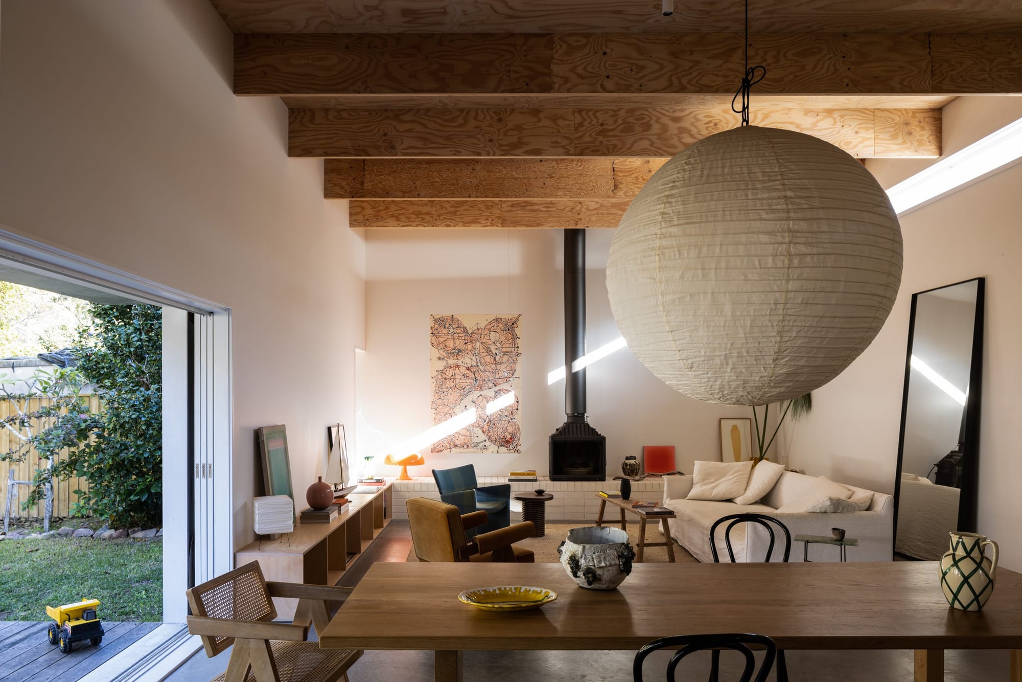 Drip-Dry House by Marker Architecture & Design. Photographed by Simon Whitbread. Ceiling with wooden panelling. living room with fireplace. White walls and white couch with wooden dining set.