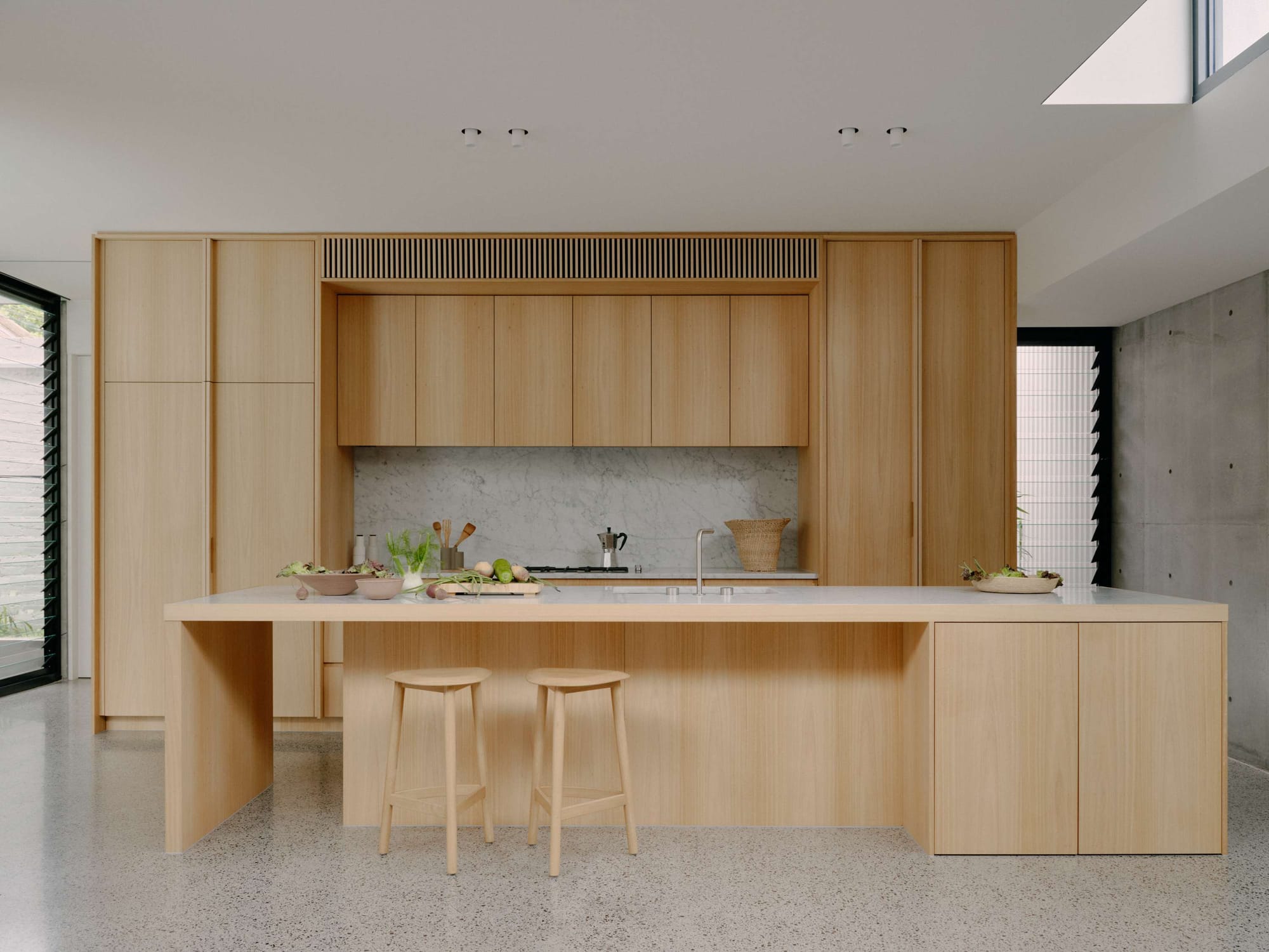 Minimalist kitchen with pale timber cabinetry, long island bench, and marble splashback in a refined Melbourne renovation