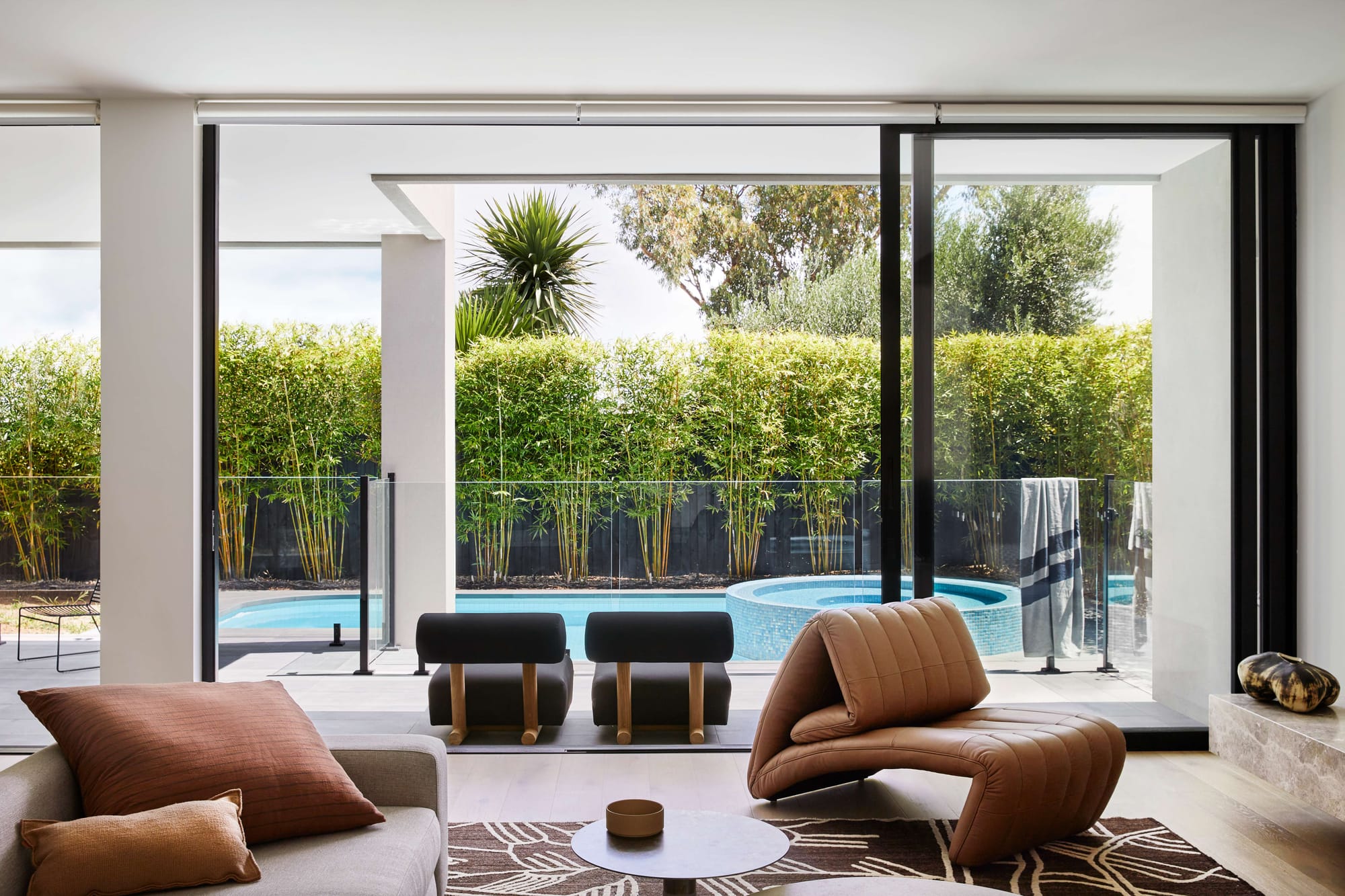 Modern living room with sculptural lounge chair and full-height glass doors opening to a pool, featured in a luxury Melbourne renovation