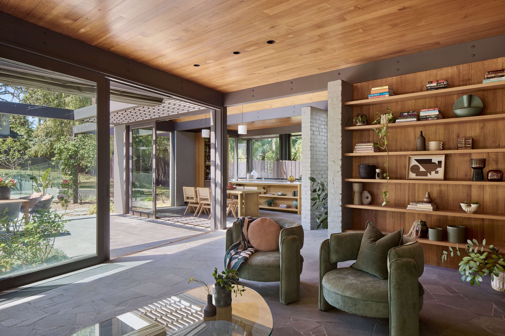 Open-plan living space with timber ceiling, green armchairs, and large glass doors to a garden, showcasing a stylish Melbourne renovation