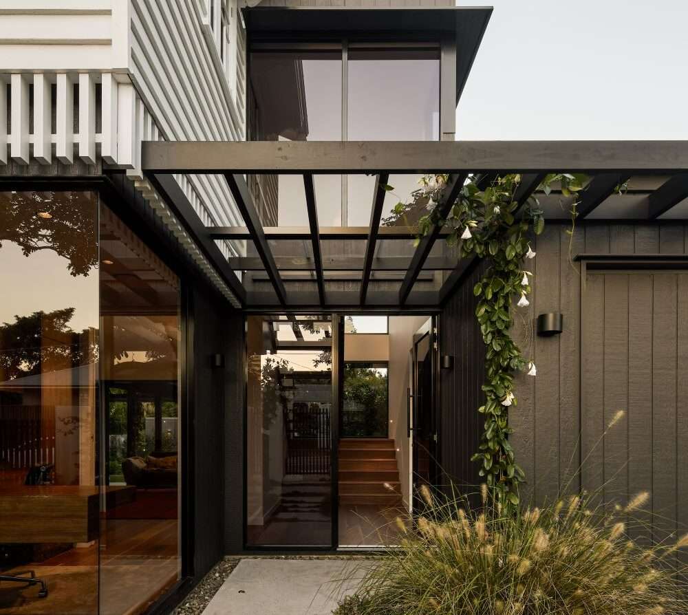 Modern home entry with glass canopy, dark cladding, and lush greenery, showcasing contemporary Brisbane renovations