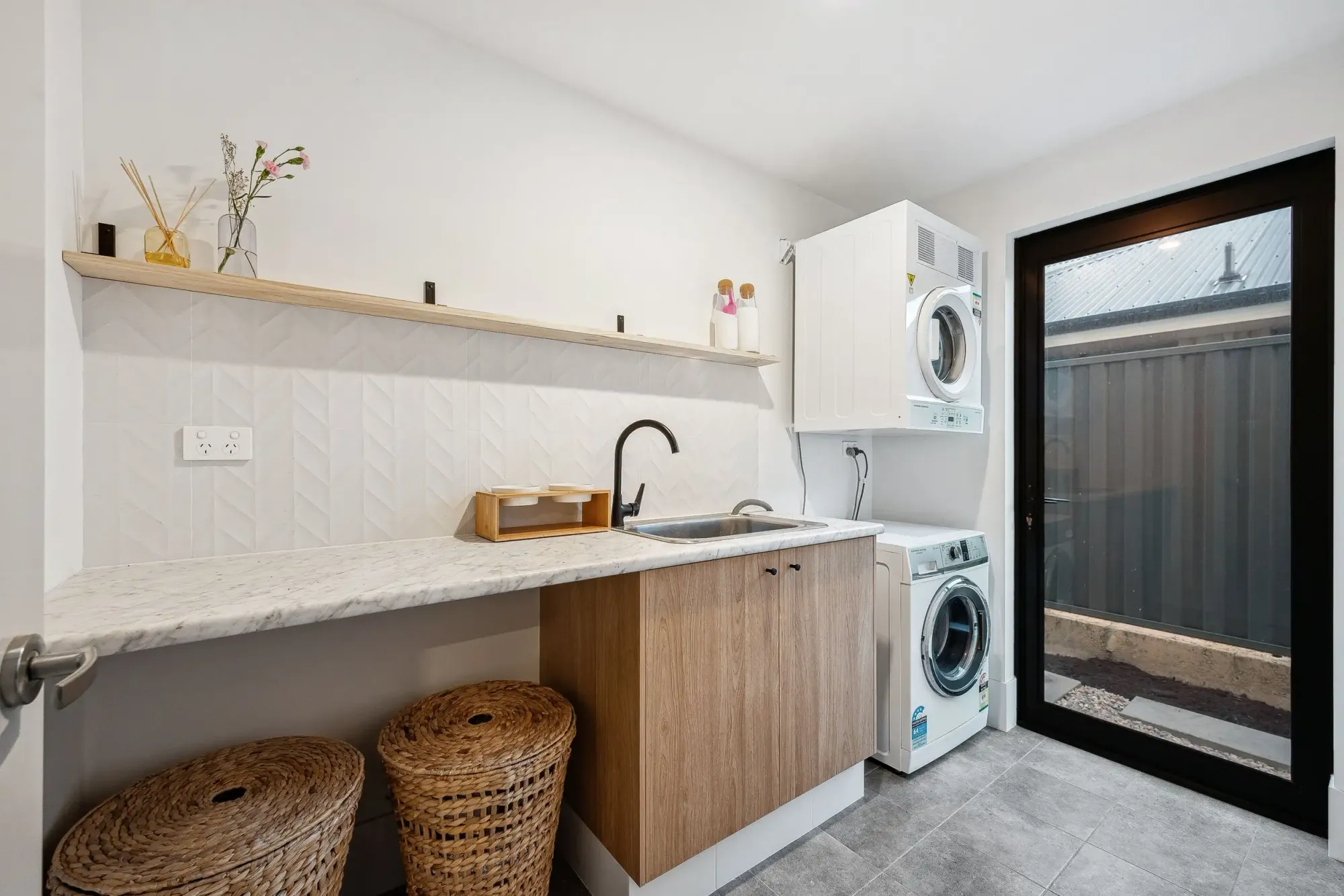 Modern laundry room with timber cabinetry, stone benchtop, and stacked washer dryer, part of a functional Perth renovation