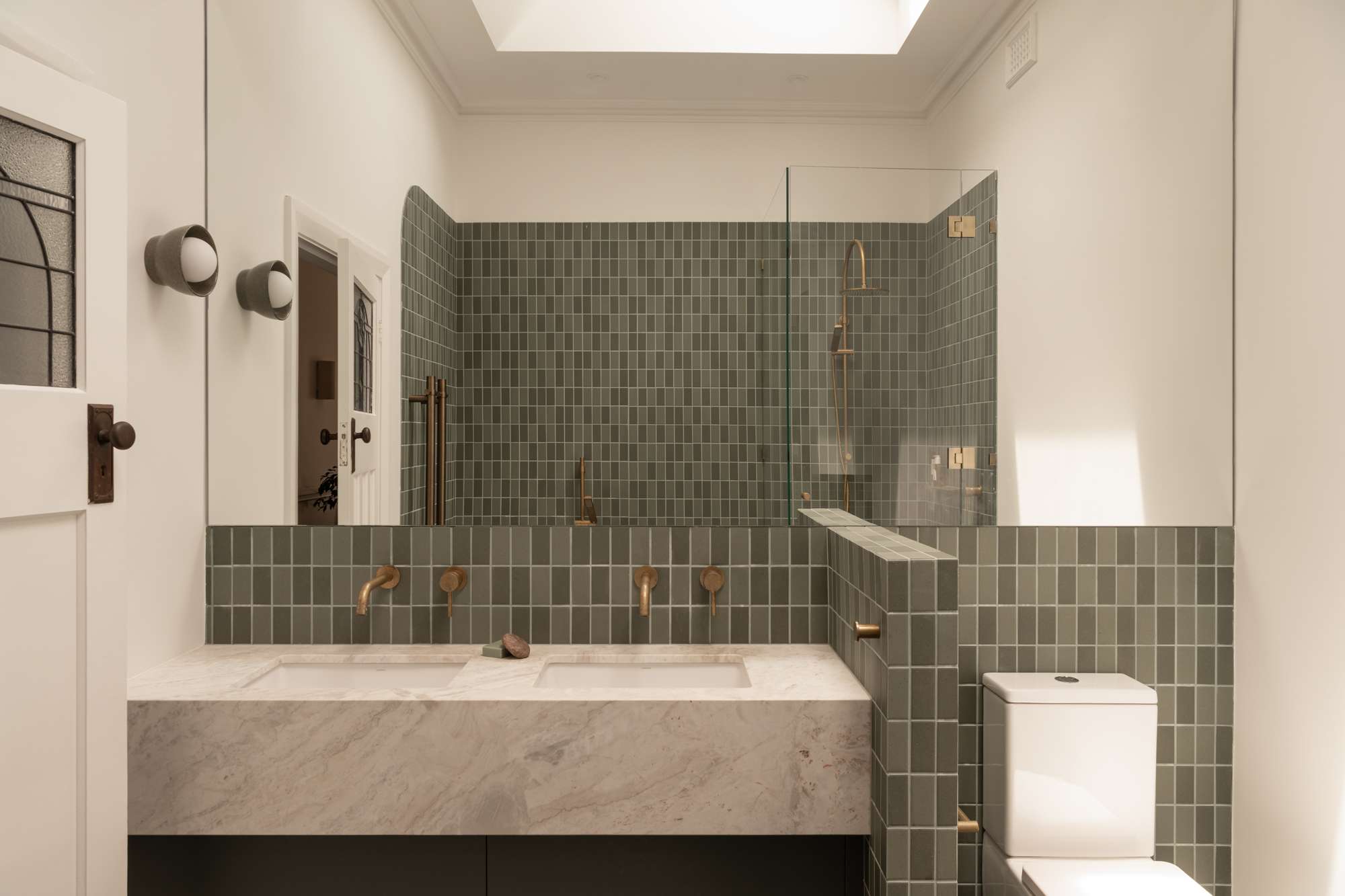 Contemporary bathroom with green tiled walls, double vanity, and brass fixtures, featured in a stylish Perth renovation