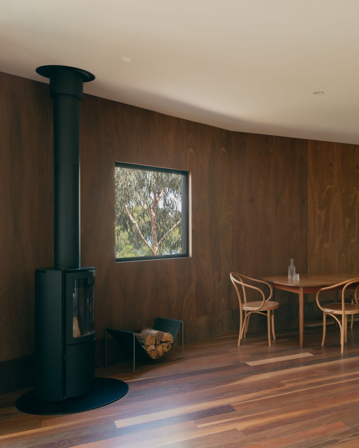 Kennett River House by MGAO showing timber interior with feature fireplace and window