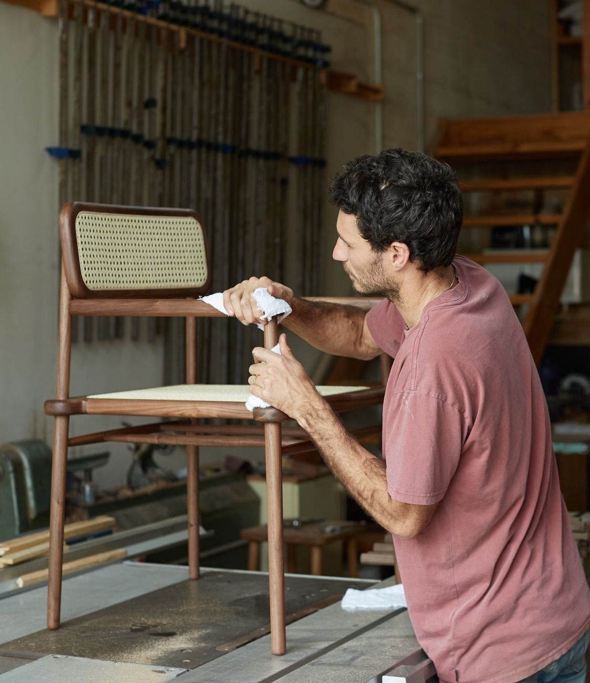  Jeremy Lee founder of JD Lee Furniture finishing a wooden chair with woven backrest in his woodworking workshop. The workspa