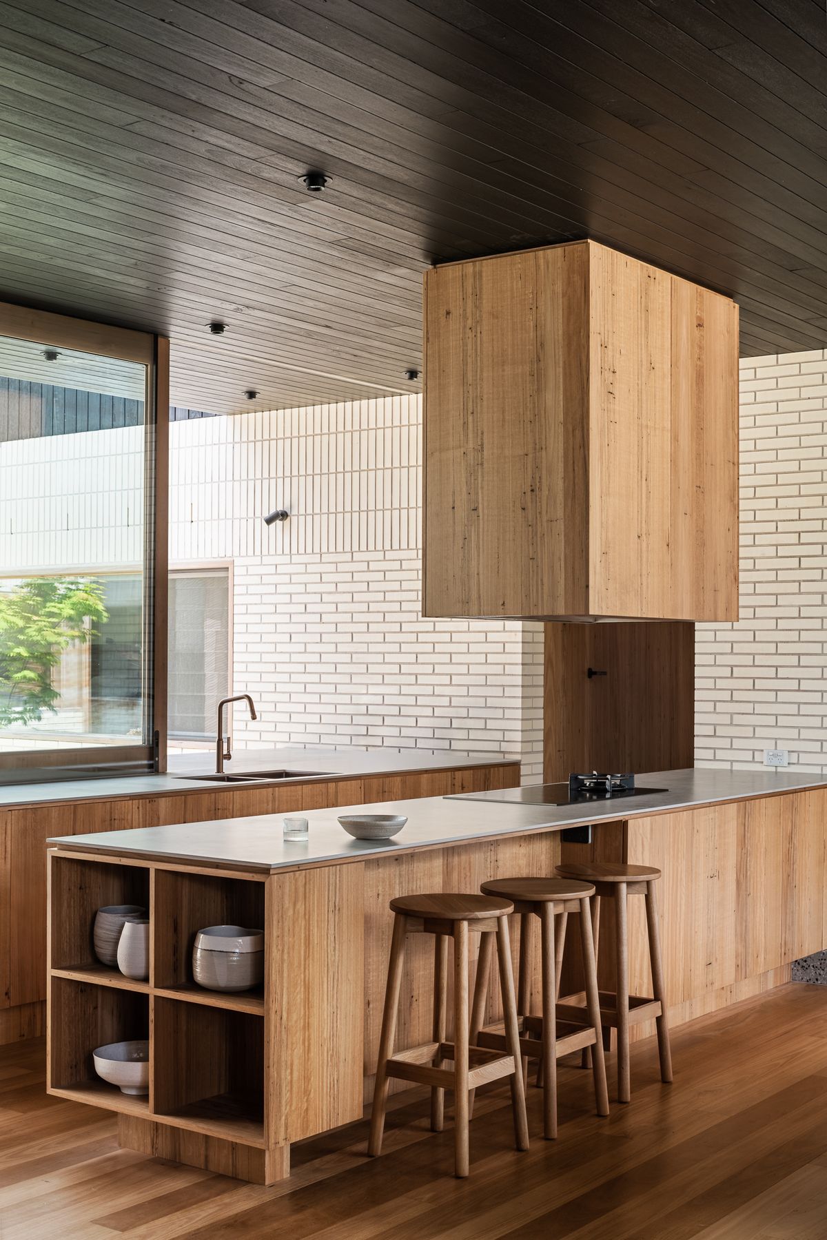 A timber veneer kitchen island with a slim benchtop and space for timber stools