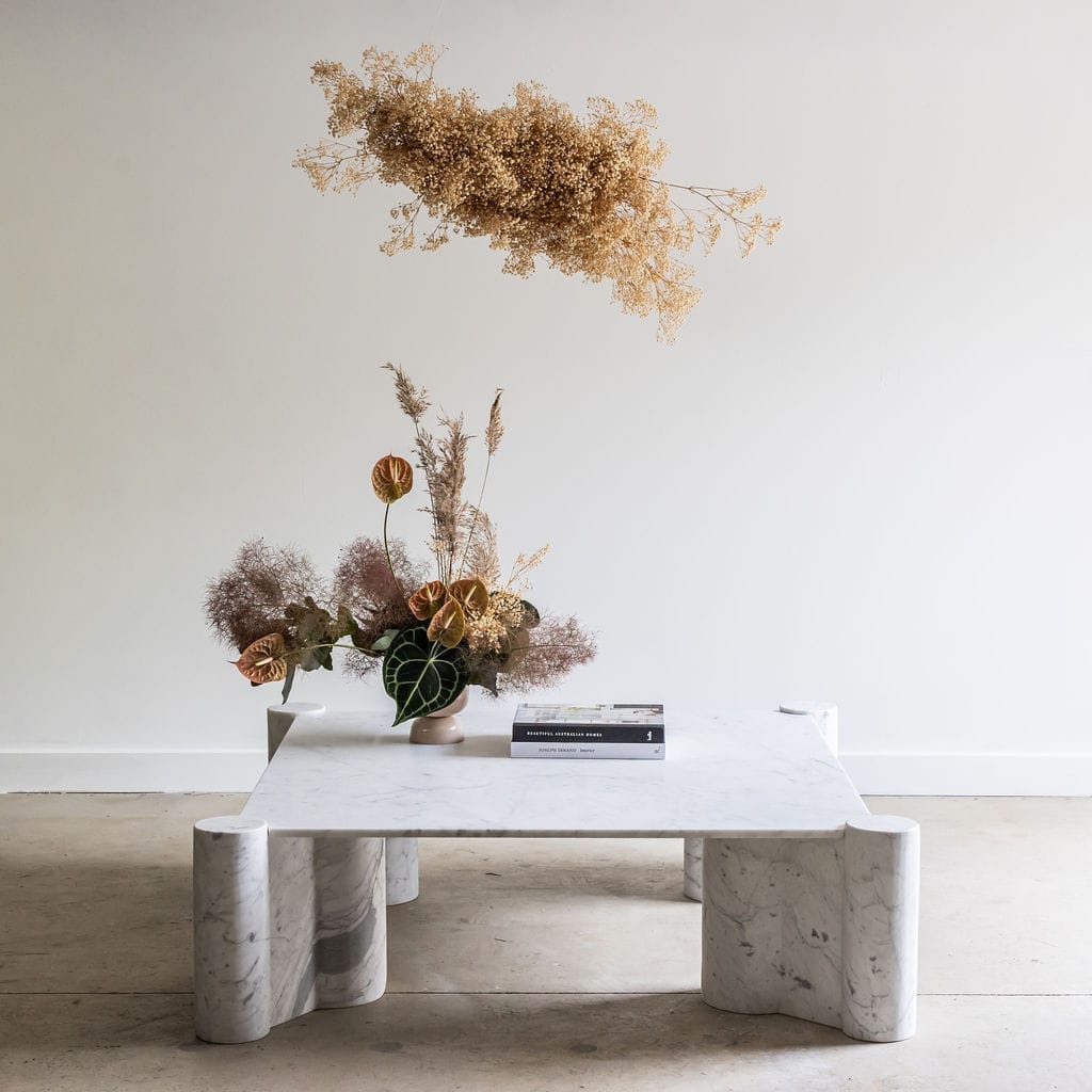 Large, rectangular white marble coffee table with round legs. Styled with an arrangement of oversized dried flowers.  