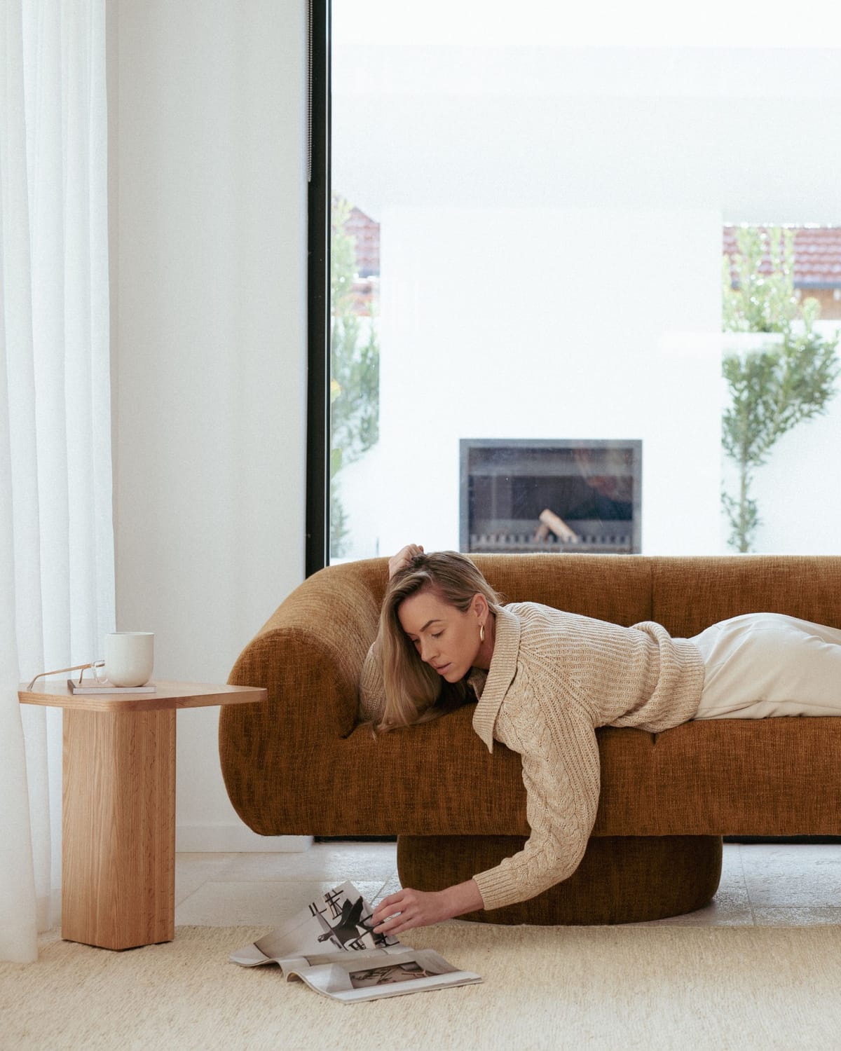 A model laying on a Made Furniture sofa reading a magazine with a timber side table to the side and a cream rug