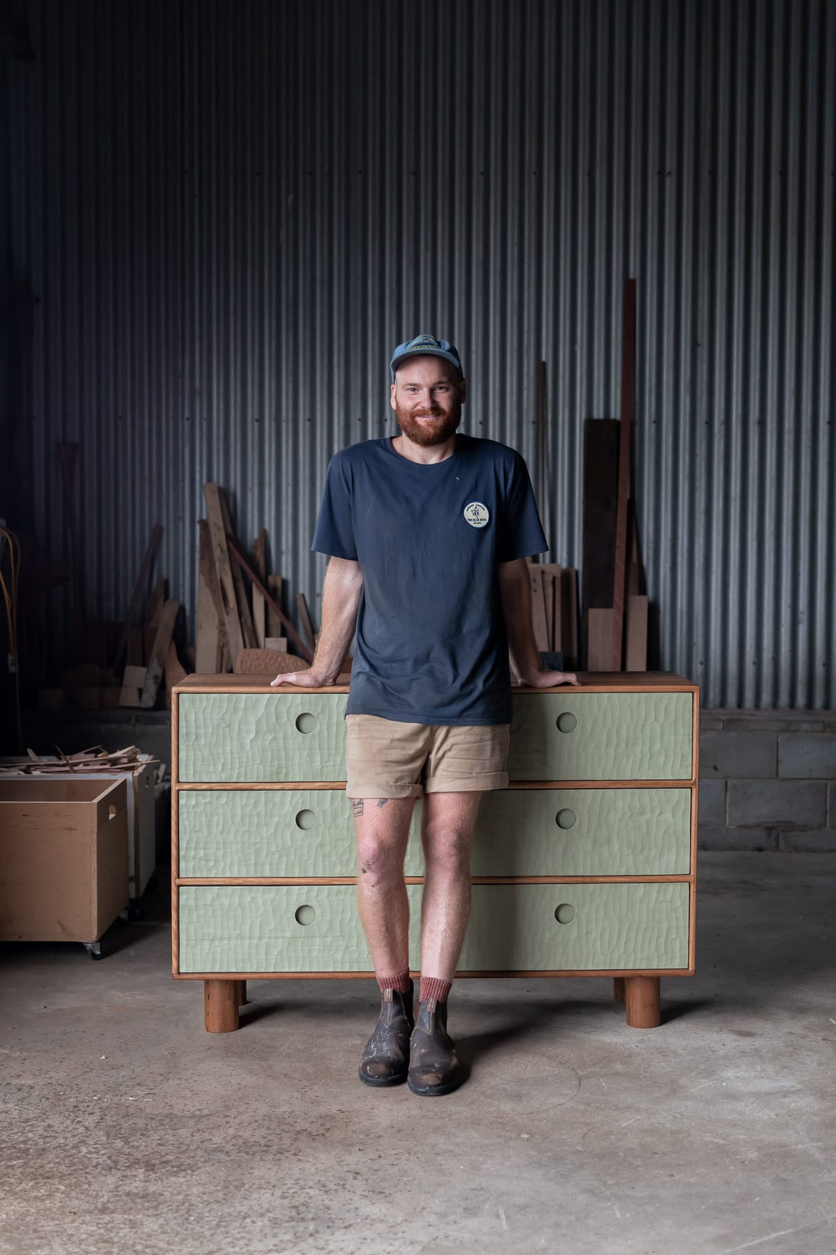 Two Blue Boys. David Steven leaning against his timber sideboard, smiling.