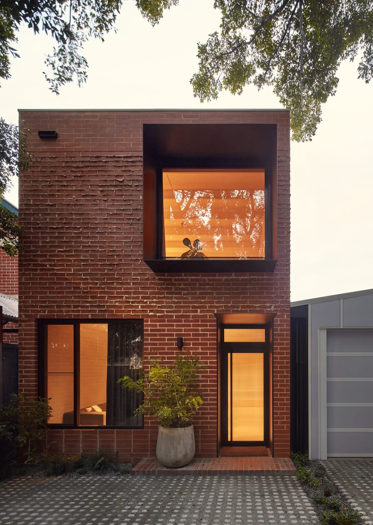 Double storey brick facade of home with large window boxes on ground and first floor with Warm lighting coming 